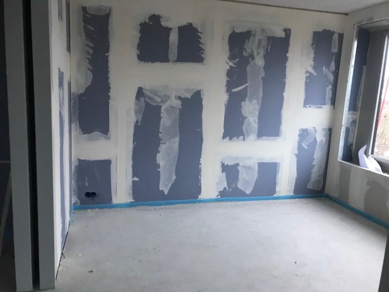 Pokój w trakcie przygotowania do malowania: częściowo nałożona warstwa wyrównująca na niebieskich płytach, zabezpieczenie podłogi niebieską taśmą malarską.