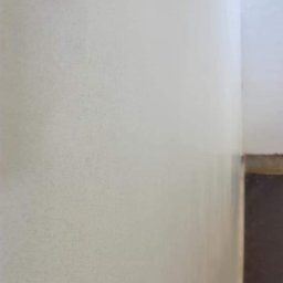 Usługi ogulno budowlane Arkadiusz Filipiak - Świeżo położona, jasna gładź szpachlowa na ścianie w rogu pomieszczenia, widoczne delikatne nierówności i struktura.