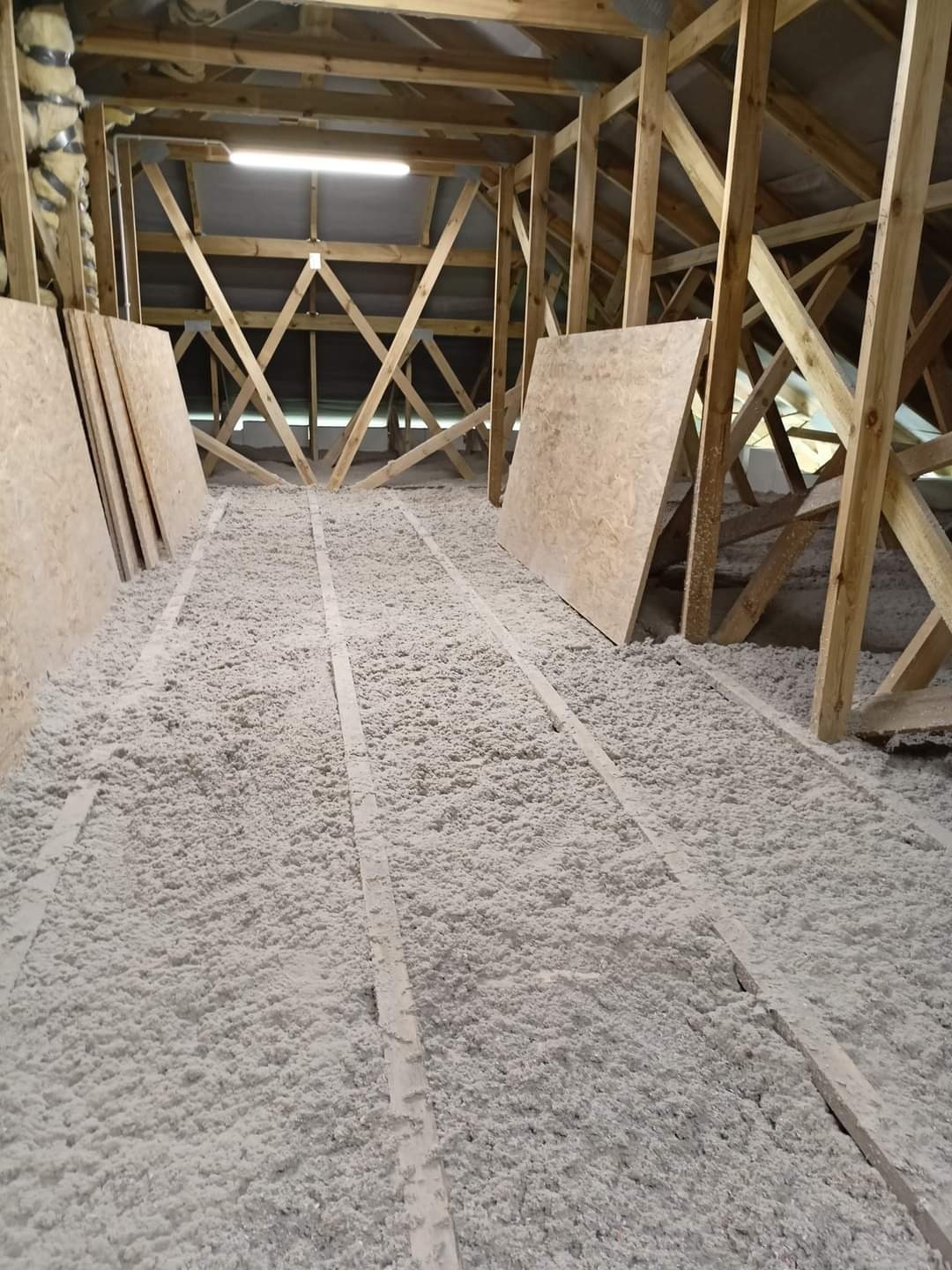 Poddasze w trakcie ocieplania, widoczne drewniane krokwie, izolacja celulozowa między legarami oraz płyty OSB przygotowane do montażu.