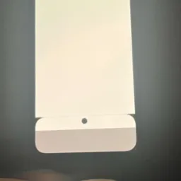 Fragment ekranu komputera stacjonarnego iMac z widocznym otworem kamery i szarą dolną częścią obudowy, sfotografowany z bliska z ręką w tle.