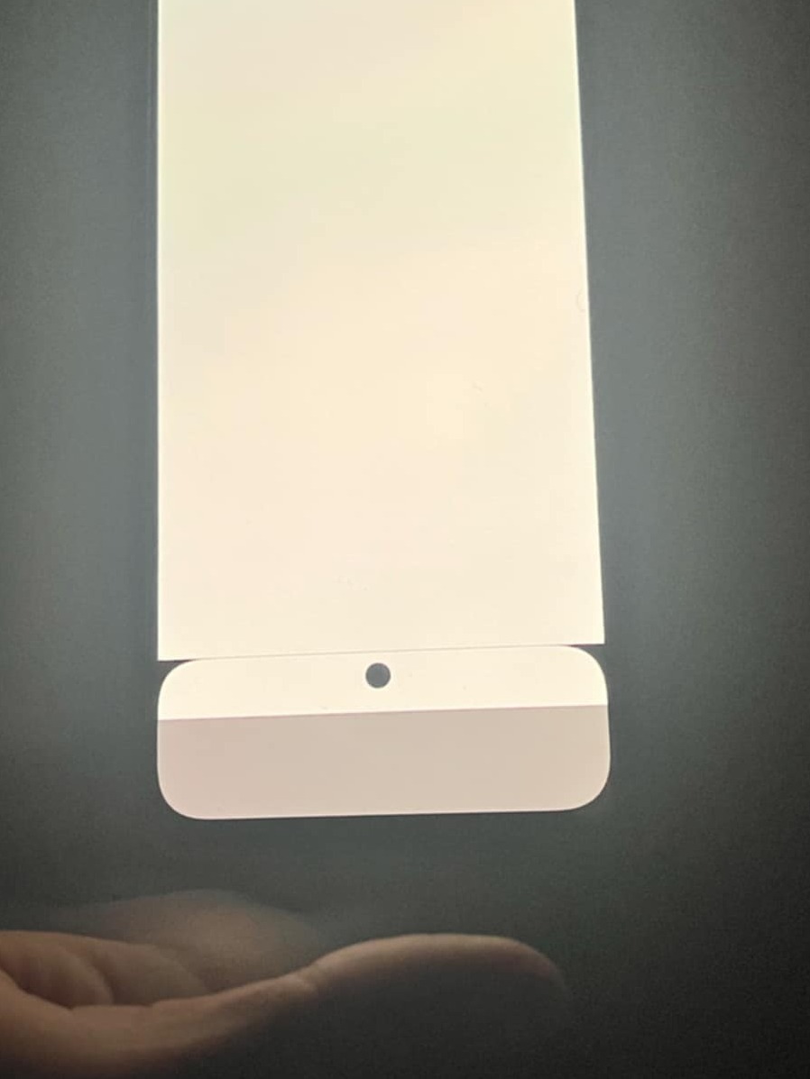 Fragment ekranu komputera stacjonarnego iMac z widocznym otworem kamery i szarą dolną częścią obudowy, sfotografowany z bliska z ręką w tle.