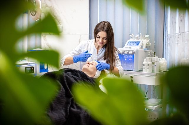 Zabieg mezoterapii igłowej wykonywany przez kosmetyczkę w Tarnowie, widoczne niebieskie rękawiczki i strzykawka, w tle urządzenie kosmetyczne z podświetleniem LED.