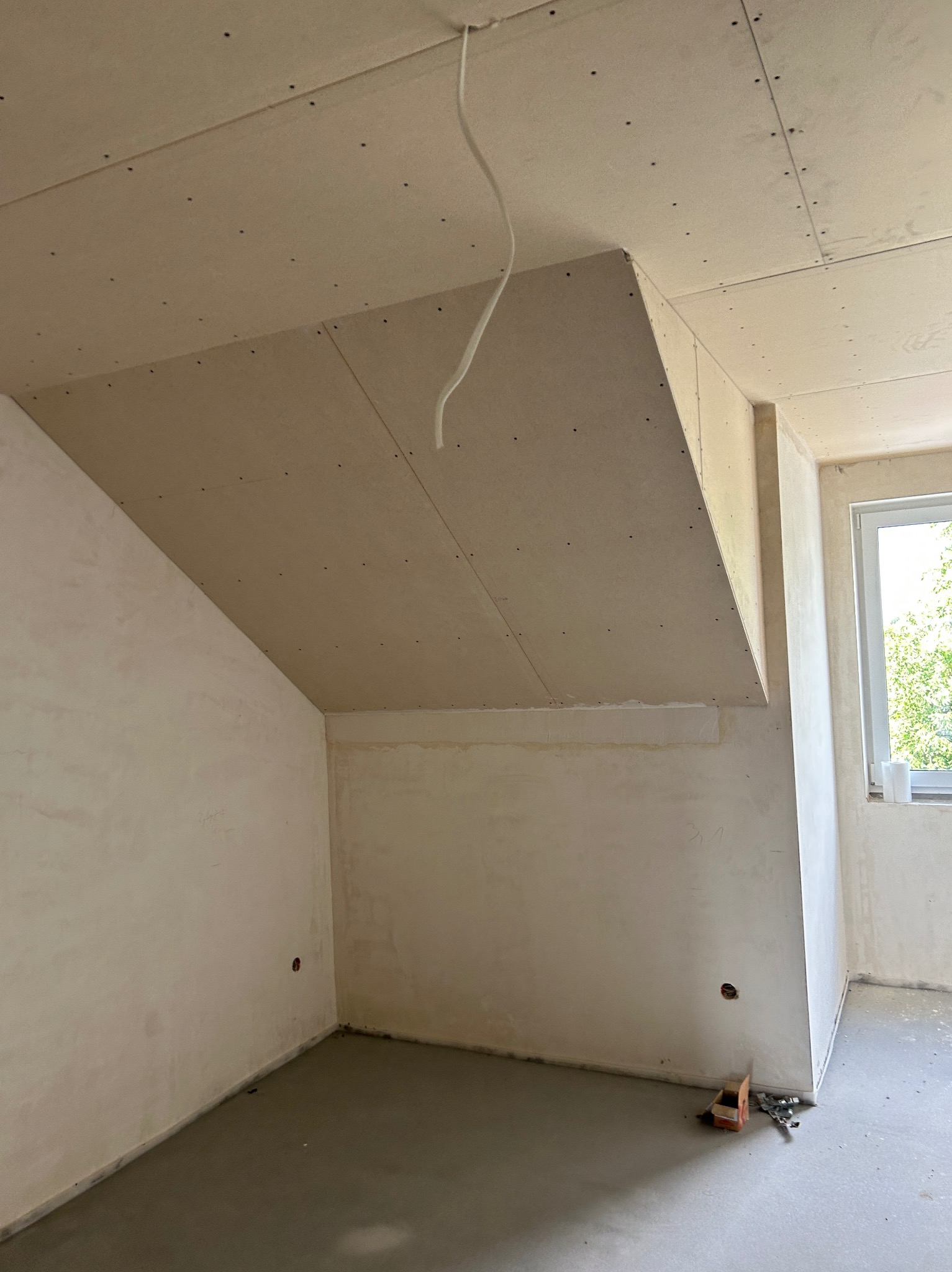 Poddasze z płytami gipsowo-kartonowymi na skośnym suficie i ścianach, przygotowane do dalszych prac wykończeniowych. Widoczne kable i niedokończone ściany.