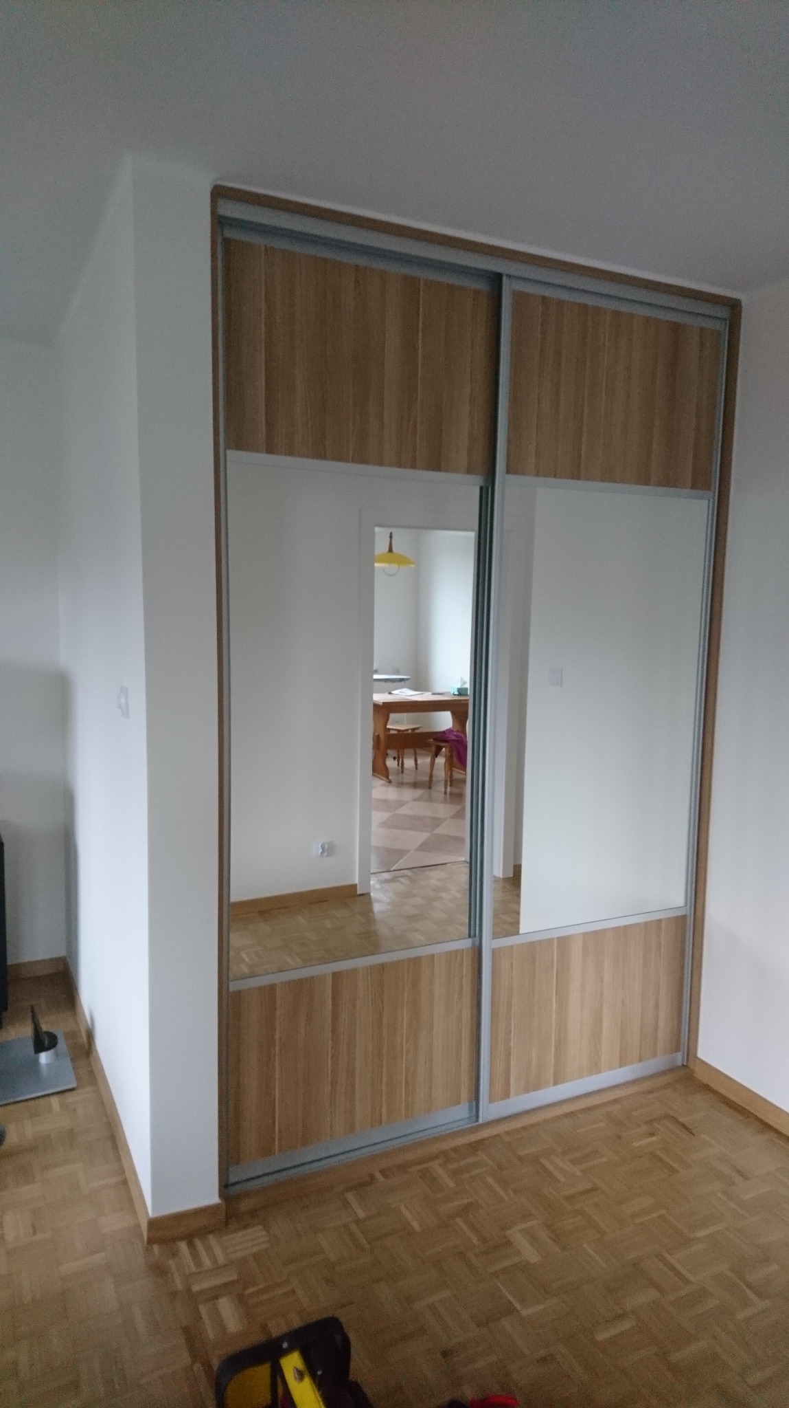 Szafa wnękowa z przesuwnymi drzwiami, drewno i lustro, widok na wnętrze pokoju z parkietem i stołem