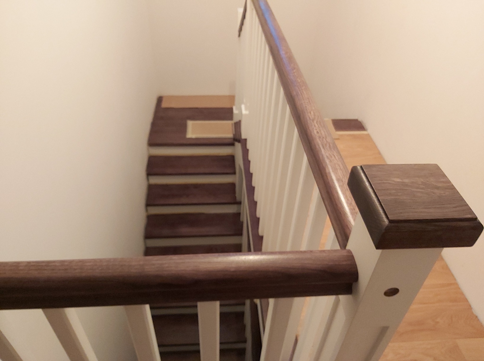 Nowoczesne schody z ciemnego drewna z białymi balustradami, widok z góry na dół, fragment podłogi zabezpieczony kartonem.