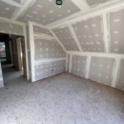 Instalacje elektryczne Zeus - Pokój na poddaszu w trakcie remontu, ściany i sufit pokryte płytami gipsowo-kartonowymi, z widocznymi łączeniami wypełnionymi szpachlą. Podłoga wyłożona płytami OSB. Widoczne kable elektryczne...