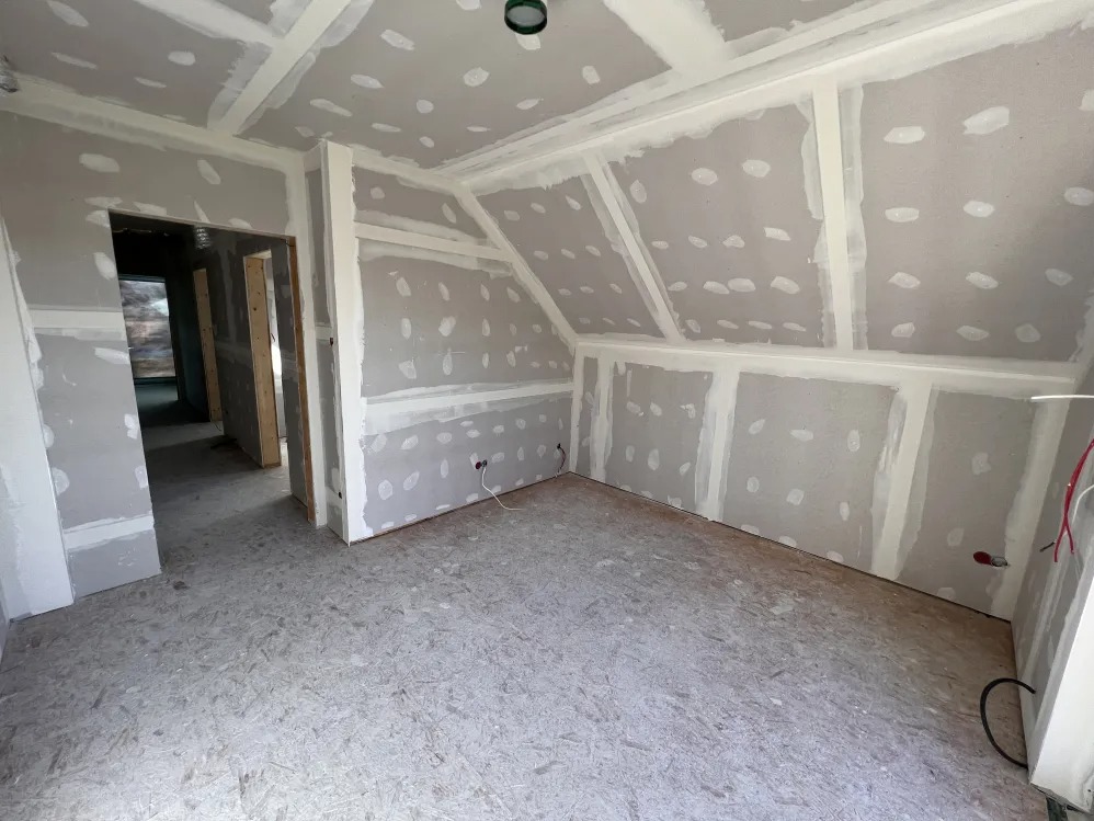 Pokój na poddaszu w trakcie remontu, ściany i sufit pokryte płytami gipsowo-kartonowymi, z widocznymi łączeniami wypełnionymi szpachlą. Podłoga wyłożona płytami OSB. Widoczne kable elektryczne...