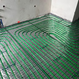 Hydro-Bud Łukasz Bulanda - Zielone rury ogrzewania podłogowego ułożone na izolacji z folią aluminiową, widok z góry, surowy stan ścian.