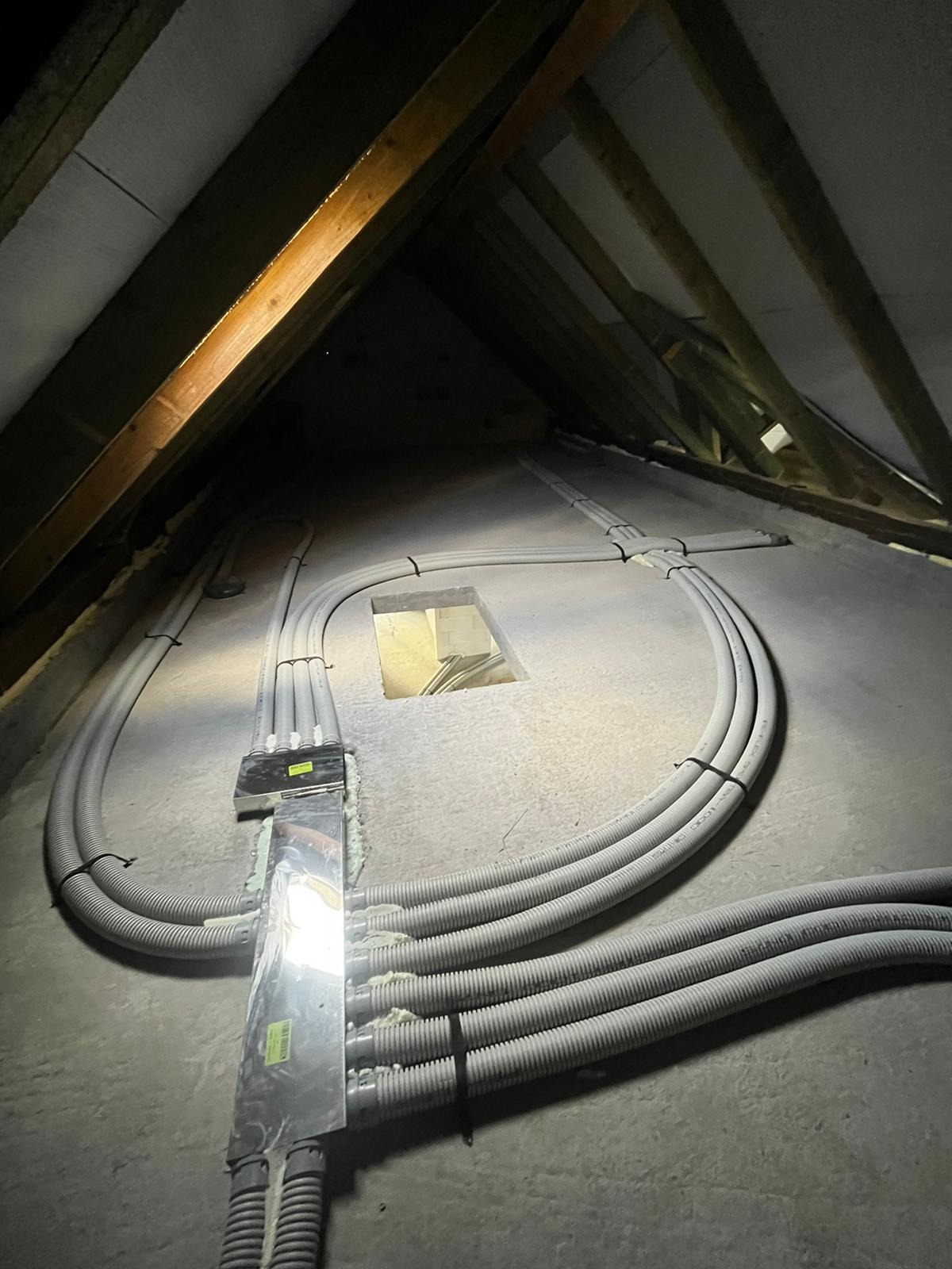 Instalacja elektryczna w peszlach na poddaszu, widoczna puszka rozdzielcza i otwór w stropie