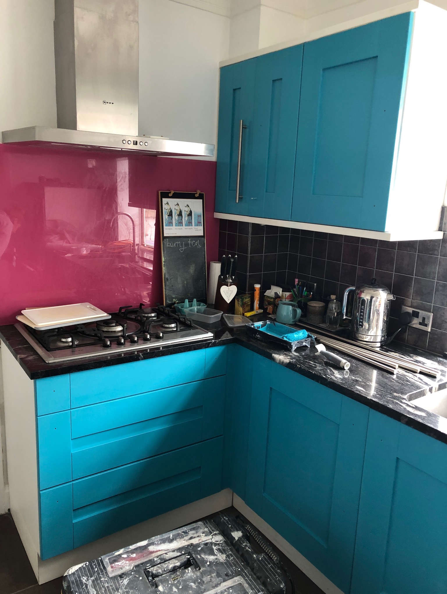 Kuchnia z turkusowymi szafkami w trakcie odświeżania, widoczny kuweta malarska z farbą, wałki i czarny blat.