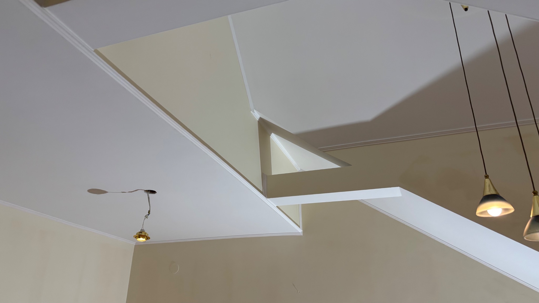 Sufit podwieszany z elementami dekoracyjnymi, widoczne fragmenty instalacji oświetleniowej i wiszące lampy z czarnymi przewodami.