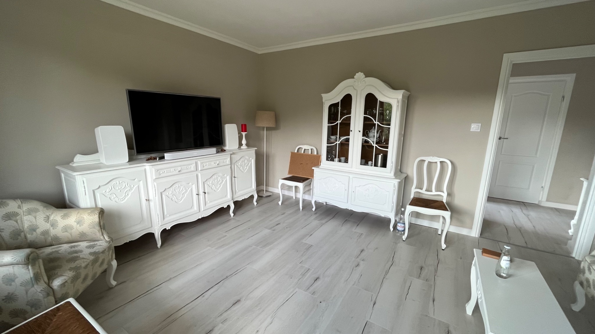 Jasne wnętrze salonu po malowaniu ścian na beżowo, z białymi meblami w stylu retro i panelami podłogowymi imitującymi drewno.