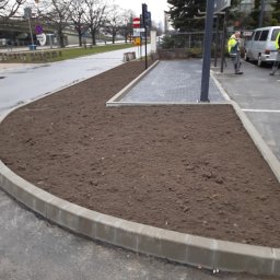julbruk - Przygotowany teren pod nasadzenia z obrzeżami z kostki brukowej, widoczny fragment chodnika z kostki i ekipa w tle.