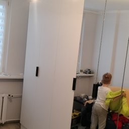 Sławek Kozik - Nowoczesna biała szafa z lustrzanymi drzwiami w pokoju, widoczny chłopiec w odbiciu.
