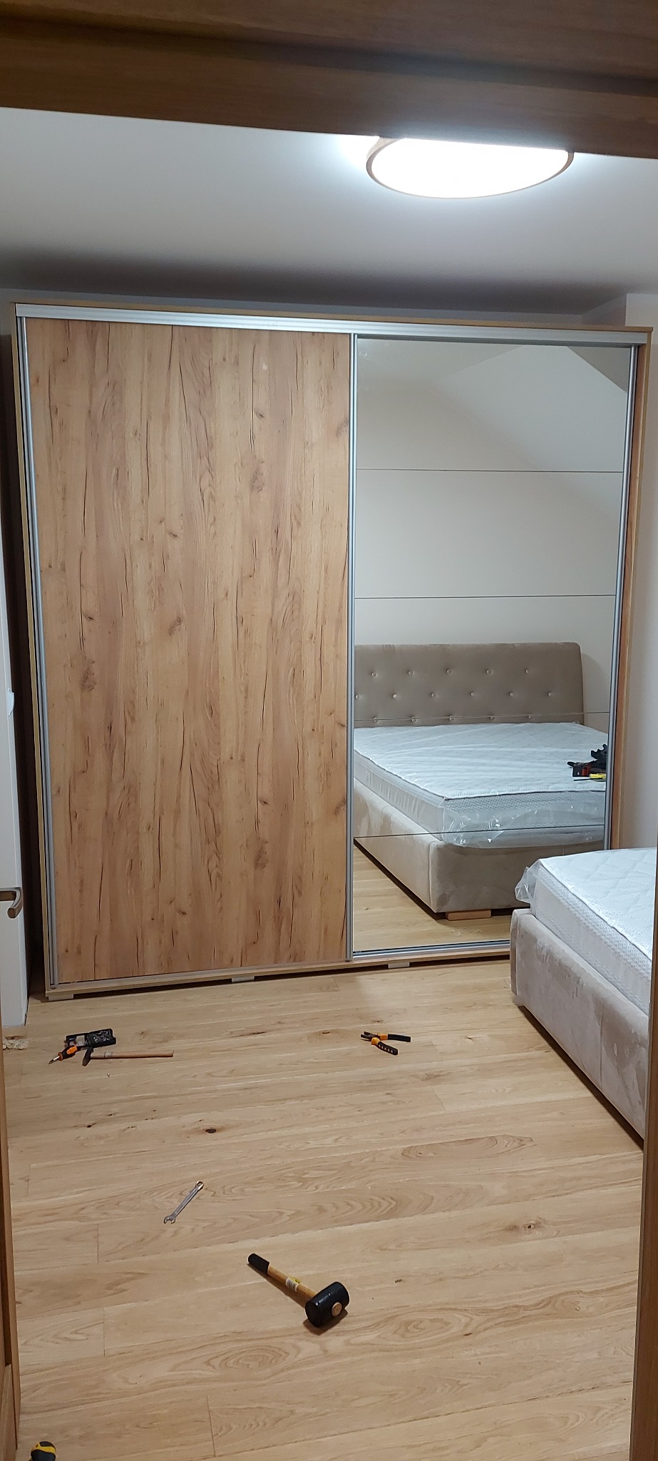 Wnętrze sypialni z zamontowaną szafą przesuwną z lustrem, narzędzia leżące na podłodze sugerują trwający montaż.