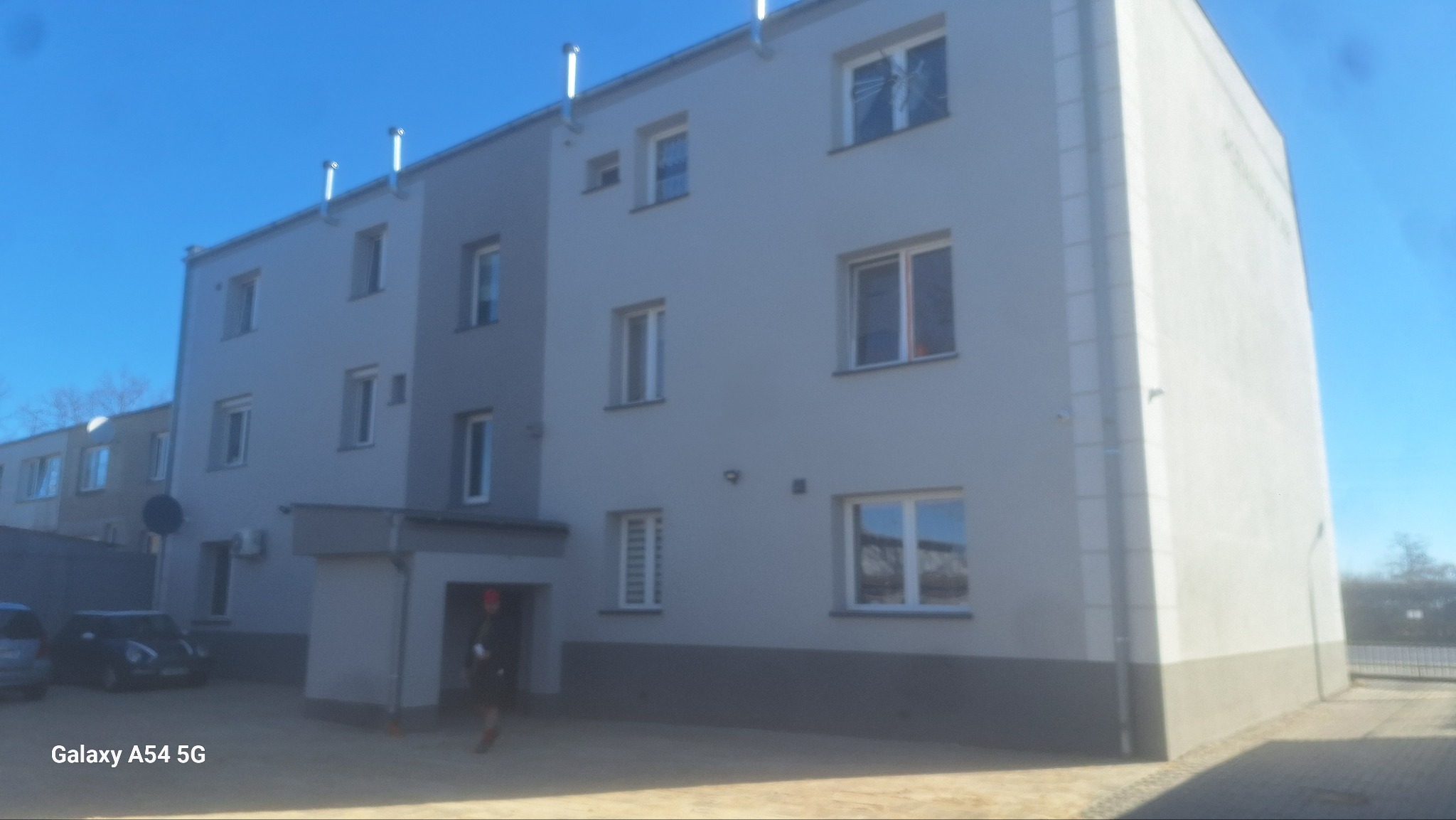 Ocieplona kamienica z nową elewacją w odcieniach szarości, z widocznymi kominami wentylacyjnymi i kostką brukową na podwórku, sfotografowana w słoneczny dzień.