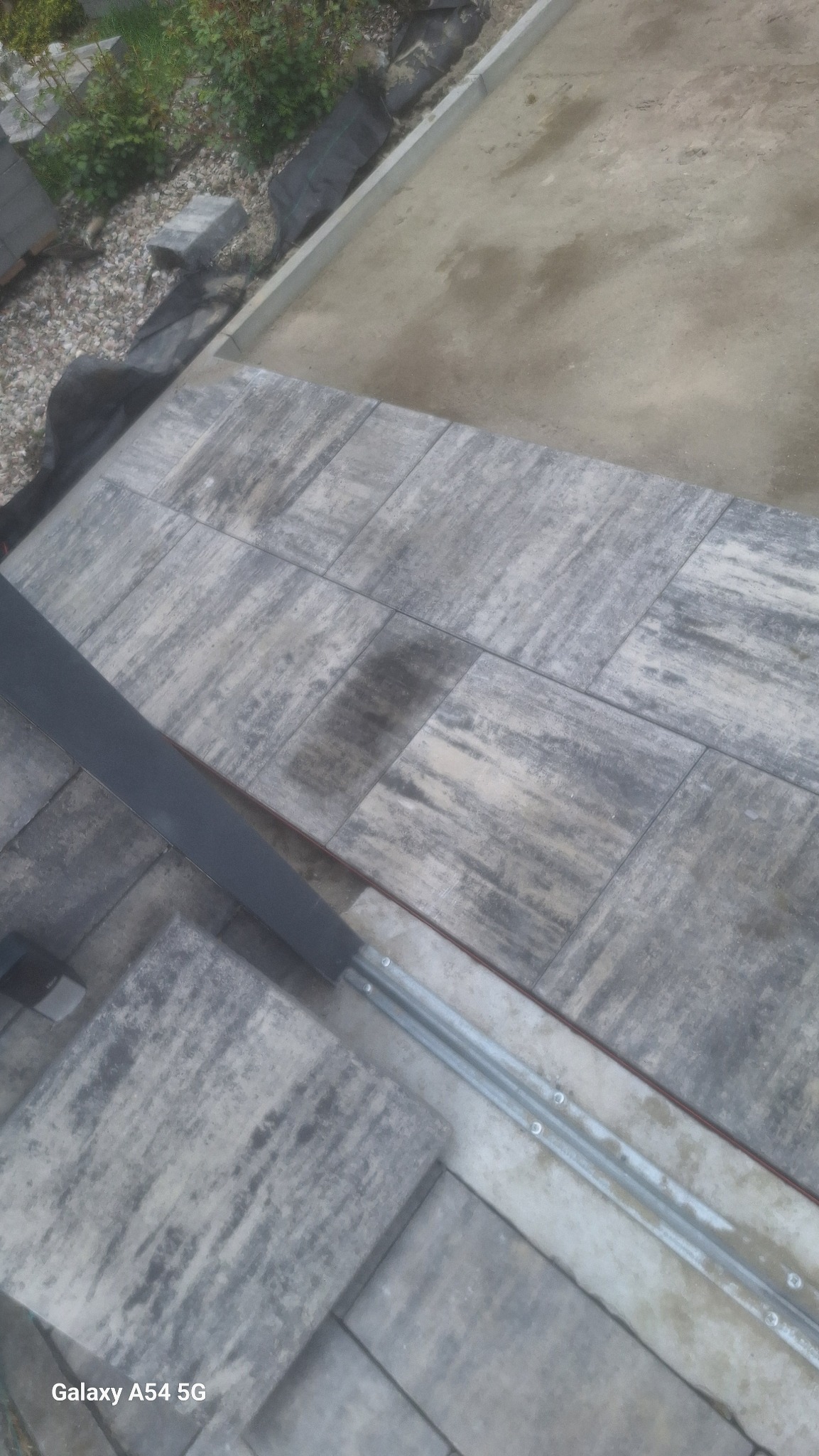 Układanie kostki brukowej z fugami w Inowrocławiu. Widok z góry na szare, prostokątne elementy z widoczną strukturą, częściowo ułożone, z elementami mocującymi.