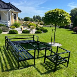 ESMET - Stelaż metalowy mebli ogrodowych w kolorze czarnym, składający się z sofy, stołu i krzesła, ustawiony na trawniku przed domem z zadbanym ogrodem w słoneczny dzień.