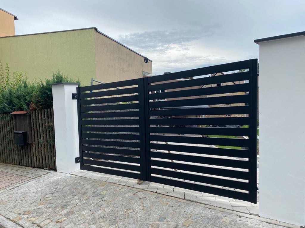 Nowoczesna, pozioma brama wjazdowa z czarnych, płaskich profili na tle kostki brukowej i białych słupków