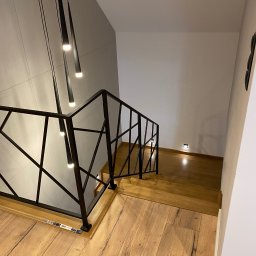 MK Elektro - Nowoczesne oświetlenie schodów z czarnymi, wiszącymi lampami i podświetleniem stopni, widok z góry na drewniane schody z czarną, geometryczną balustradą.