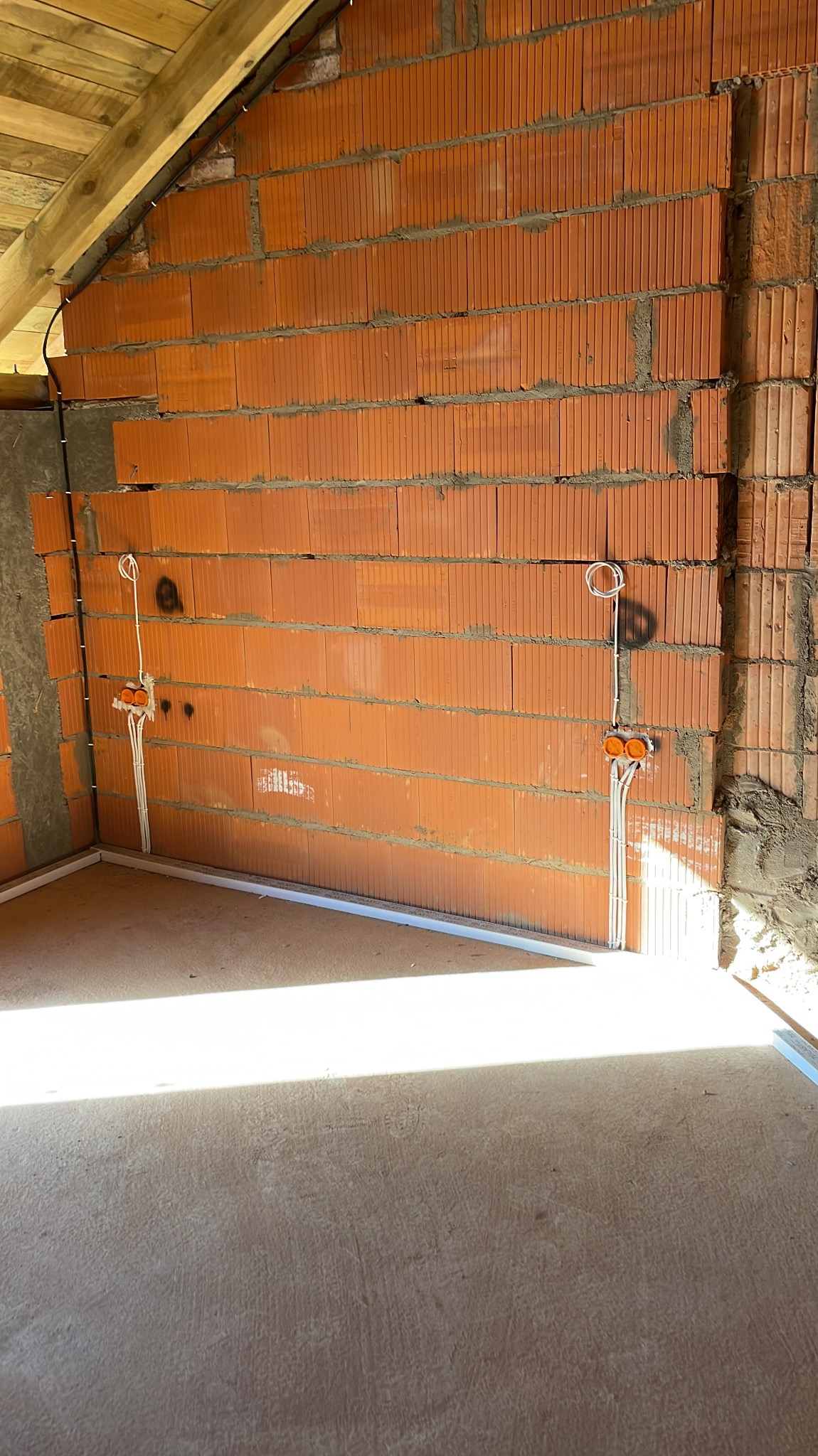 Surowy mur z pustaków ceramicznych z rozprowadzoną instalacją elektryczną: kable w peszlach prowadzone pionowo od puszek instalacyjnych, widoczne elementy konstrukcji dachu