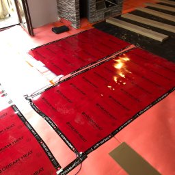 Pmbudex - Montaż folii grzewczej Dream Heat na podłodze, przygotowanie do ułożenia paneli podłogowych w nowym domu, widoczny kominek w tle.