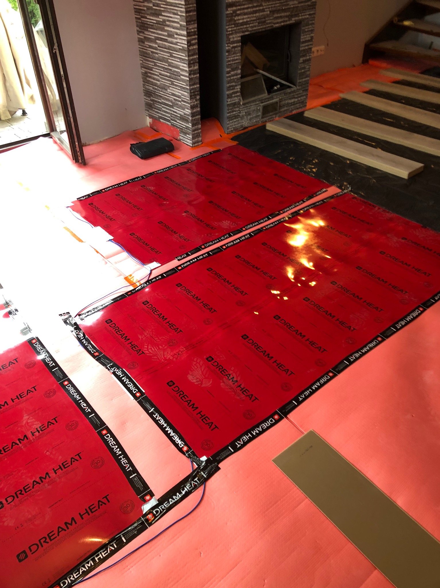 Montaż folii grzewczej Dream Heat na podłodze, przygotowanie do ułożenia paneli podłogowych w nowym domu, widoczny kominek w tle.