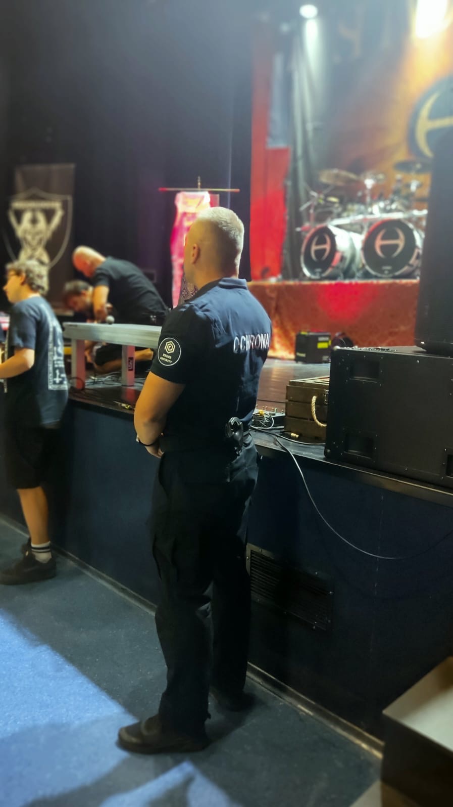 Ochroniarz w Radomiu stoi na sali koncertowej, plecami do widza, w tle scena z instrumentami i pracownikami technicznymi.