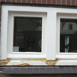 krakow-malowanie.pl - Renowacja drewnianej ramy okiennej z widocznymi śladami starej farby i nałożonym szpachlem, ceglana ściana w tle.