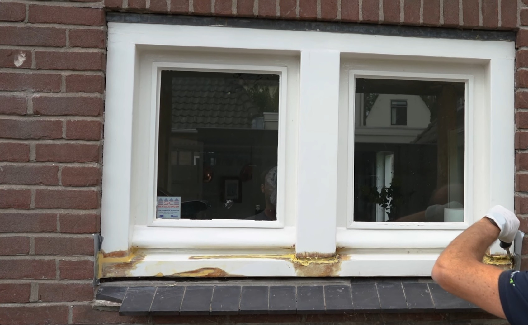 Renowacja drewnianej ramy okiennej z widocznymi śladami starej farby i nałożonym szpachlem, ceglana ściana w tle.