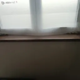 Montaż brązowego parapetu wewnętrznego w oknie dachowym, zabezpieczonym folią malarską.