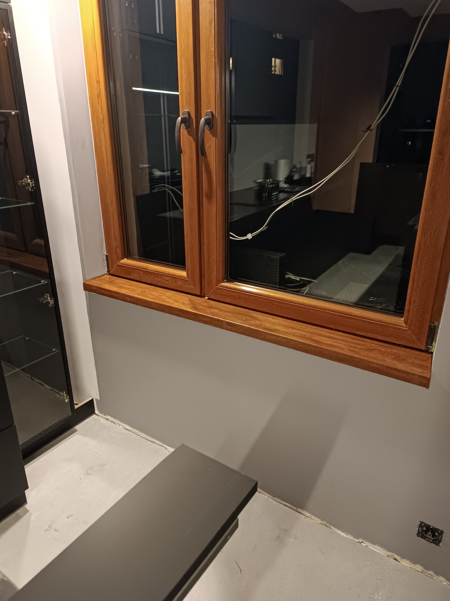 Drewniane okno z brązowym parapetem w szarym pokoju, widok na nocne miasto za oknem.