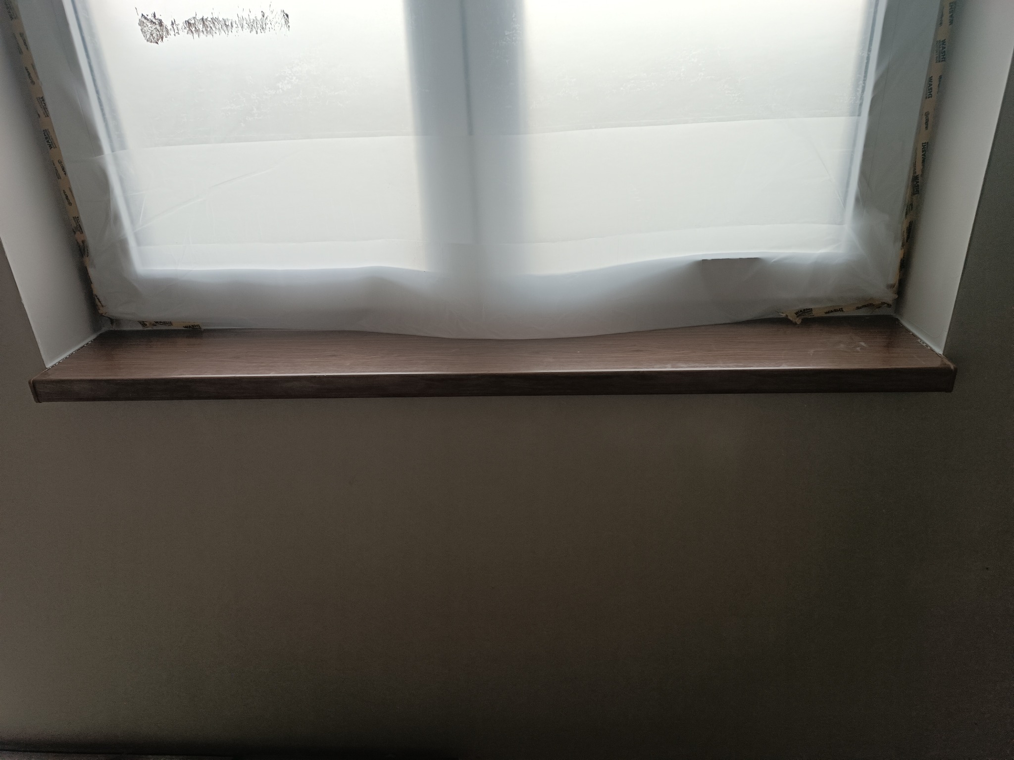 Montaż brązowego parapetu wewnętrznego w oknie dachowym, zabezpieczonym folią malarską.