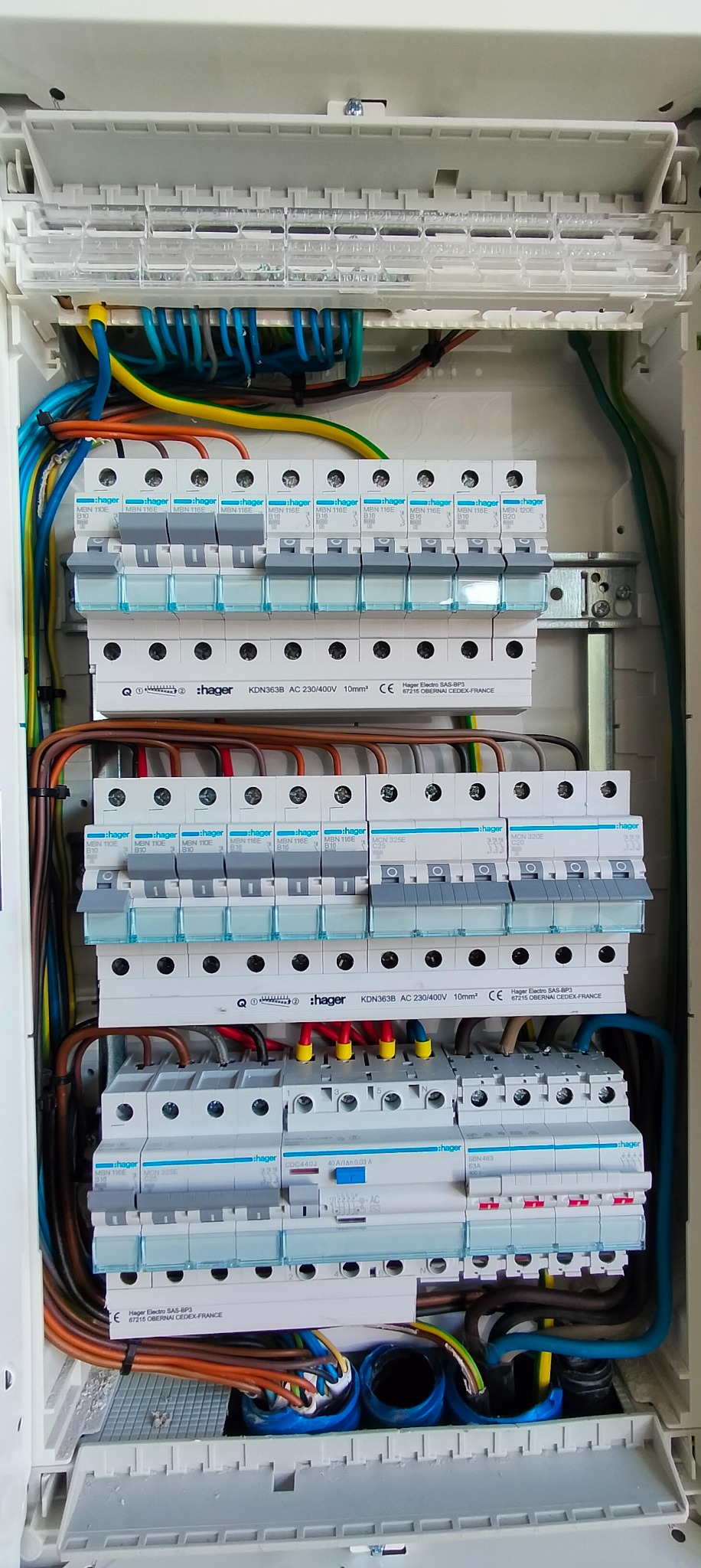 Otwarta skrzynka rozdzielcza z widocznymi bezpiecznikami Hager, okablowaniem w różnych kolorach i oznaczeniami na elementach, zamontowana wewnątrz obudowy.