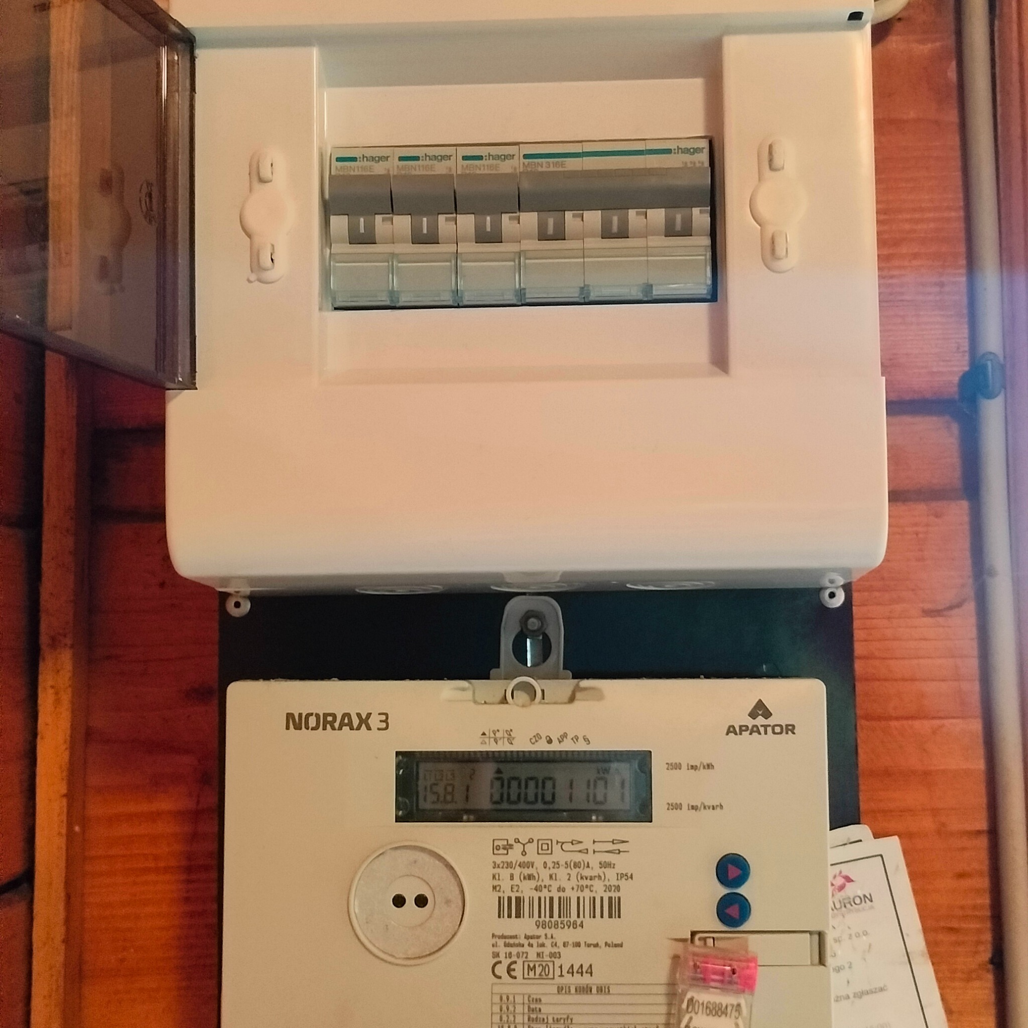 Rozdzielnia elektryczna Hager z licznikiem Norax 3 firmy Apator, widok z bliska na ścianie z boazerii.