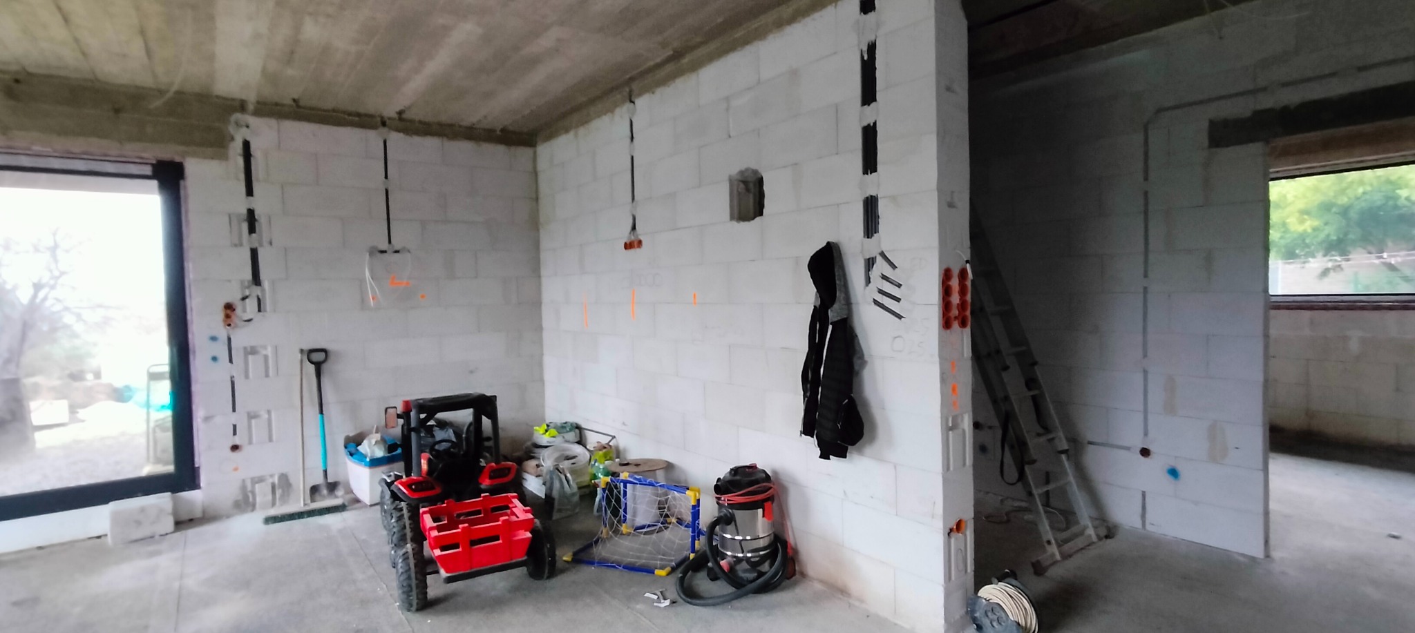 Surowy stan wnętrza w Okocimiu z widocznymi przewodami elektrycznymi w bruzdach ściennych, przygotowanymi do dalszych prac; zabawkowy traktor i inne przedmioty na podłodze.