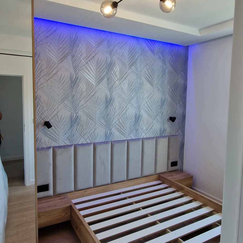 Sypialnia z drewnianą ramą łóżka, tapicerowanym zagłówkiem, wzorzystą tapetą z podświetleniem LED i nowoczesnymi lampami sufitowymi.