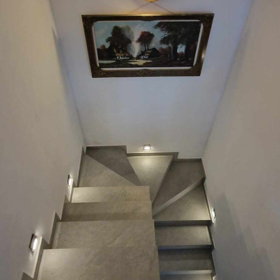 Betonowe schody z wbudowanym oświetleniem punktowym w ścianie, obraz w złotej ramie na suficie.
