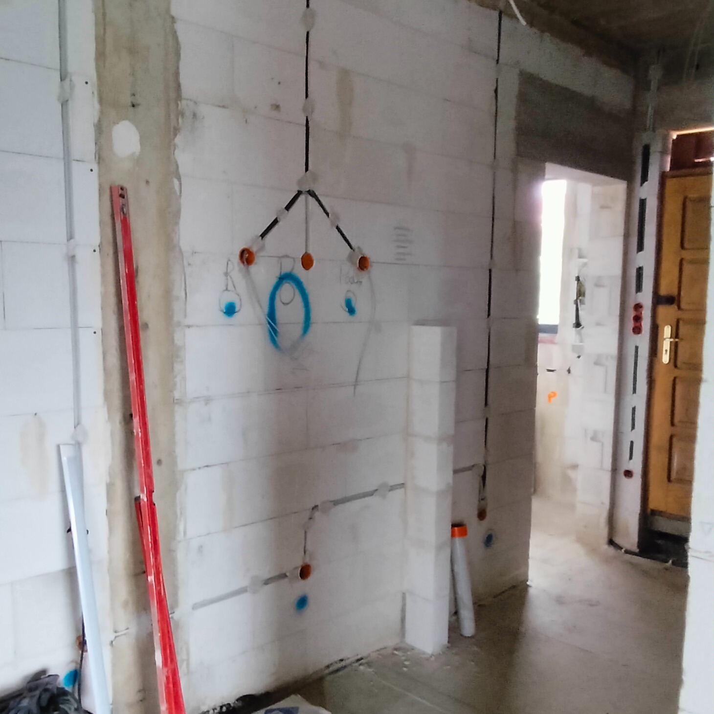 Surowy stan instalacji elektrycznej w budynku z widocznymi przewodami, puszkami i poziomnicą opartą o ścianę z betonu komórkowego.