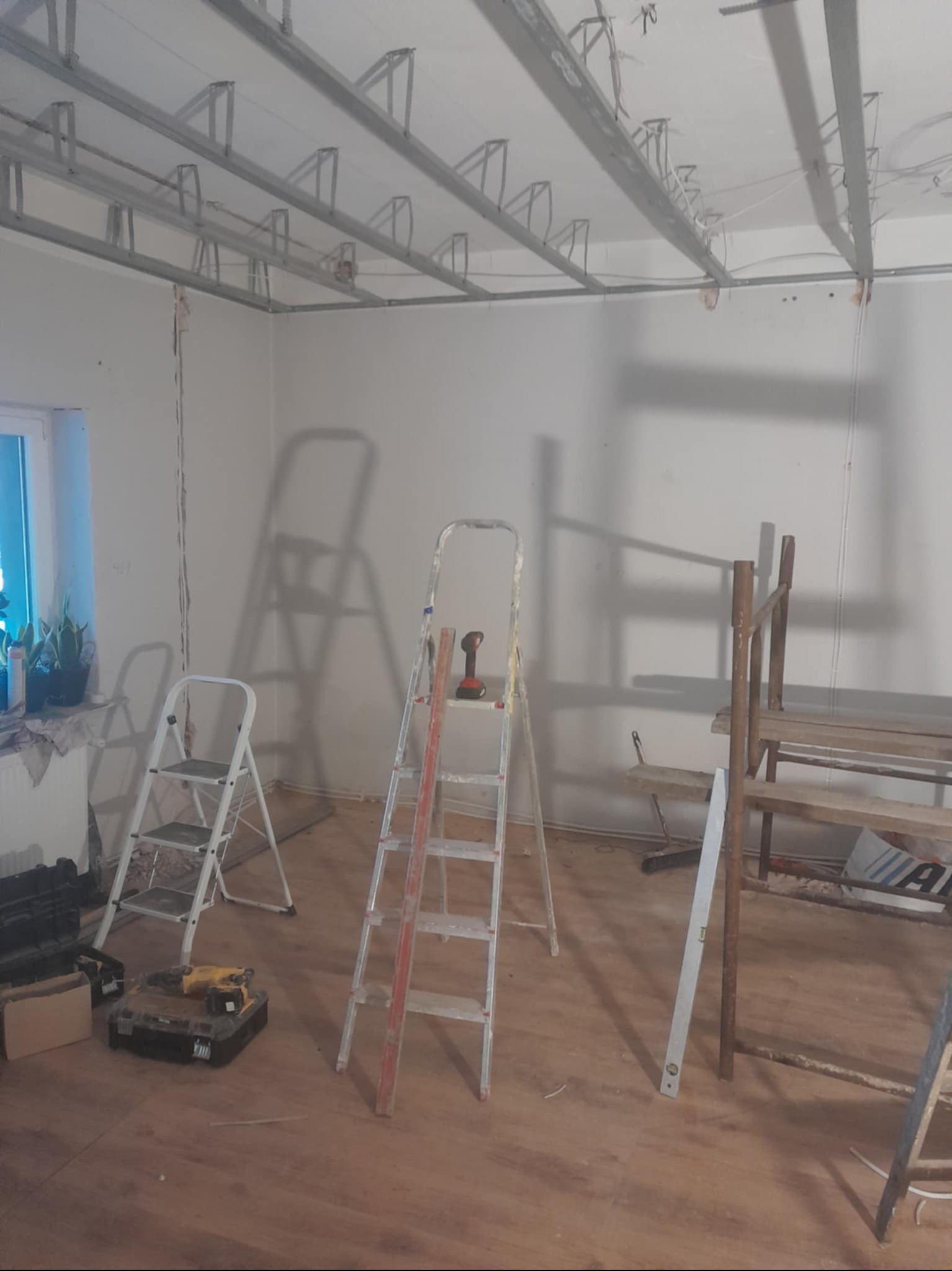Montaż metalowej konstrukcji sufitu podwieszanego w Pelplinie, widoczne drabiny, narzędzia i fragment okna.