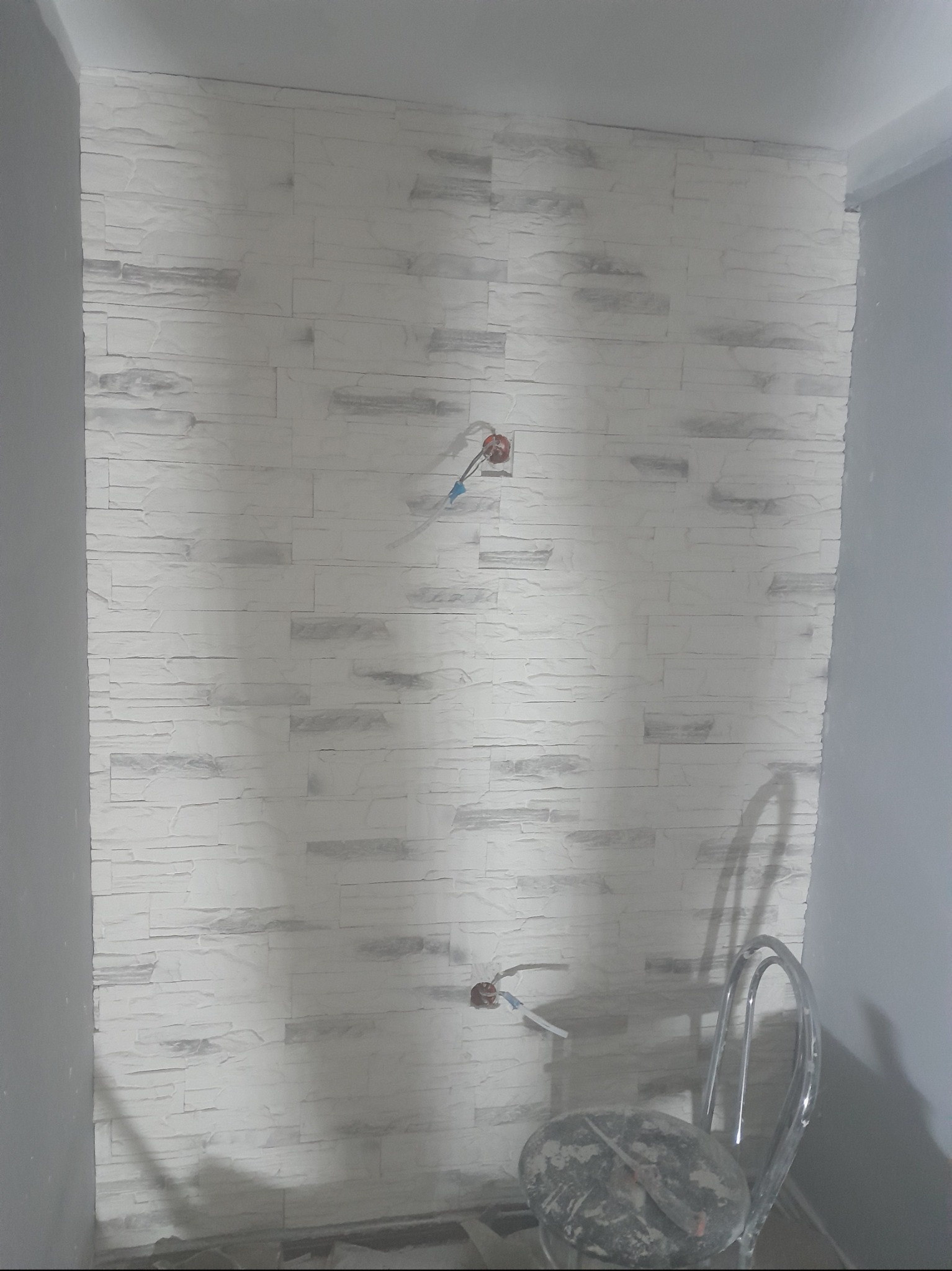 Ściana wykończona dekoracyjną okładziną imitującą kamień, widoczne puszki elektryczne i krzesło robocze.