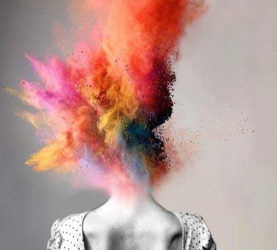 Kobieta odwrócona tyłem, z głowy której eksploduje chmura wielobarwnych proszków, tworząc abstrakcyjną kompozycję.