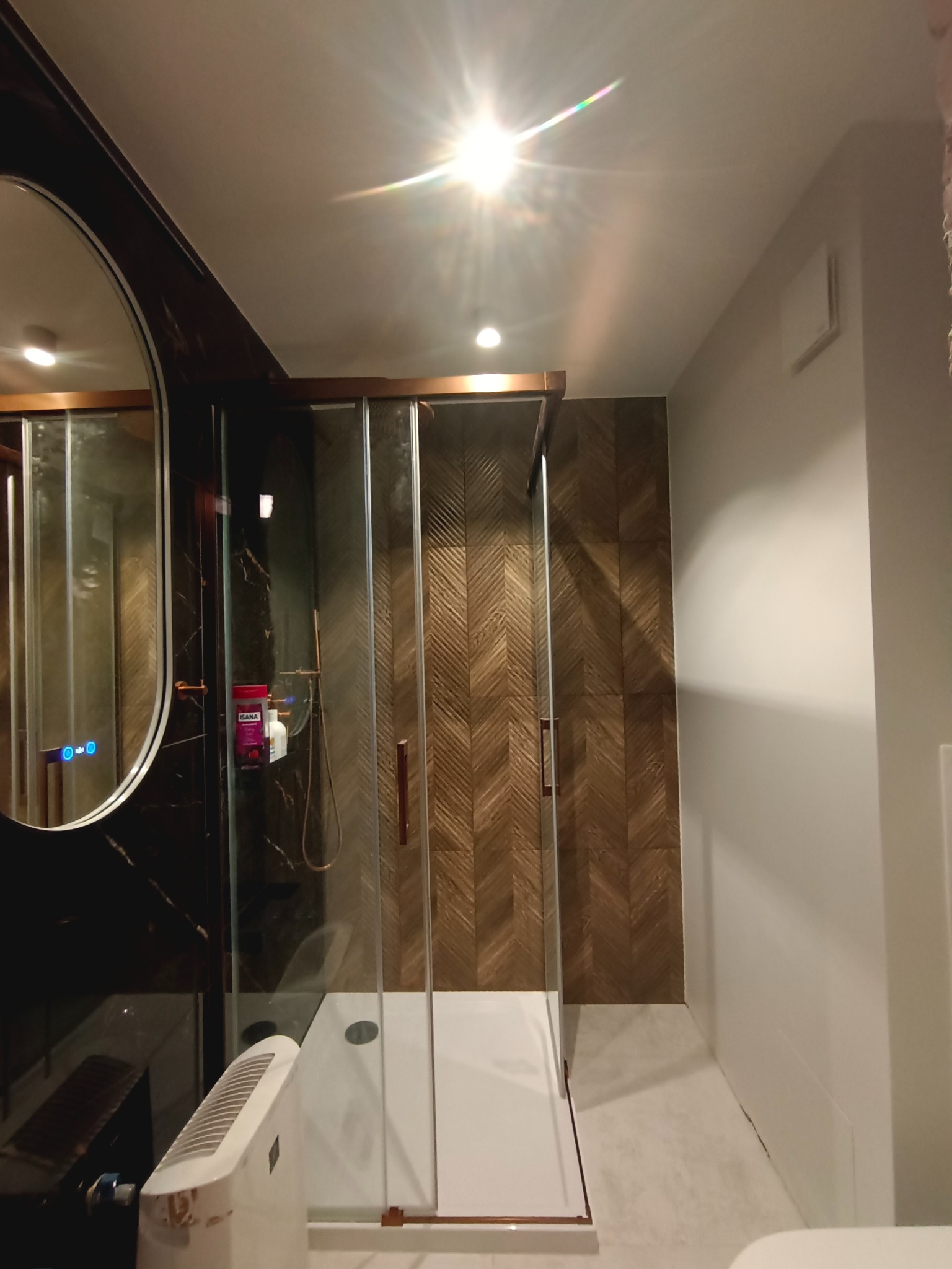 Nowoczesna kabina prysznicowa z drewnopodobnymi płytkami w jodełkę, widoczna w łazience po remoncie w Szreńsku. Lustro z podświetleniem i marmurowa ściana.