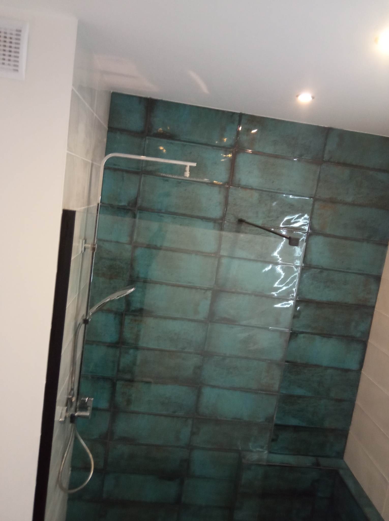 Kabina prysznicowa z turkusowymi, prostokątnymi płytkami z ciemnymi fugami, zamontowana w łazience w Warszawie. Widoczny chromowany zestaw natryskowy i szklane drzwi.