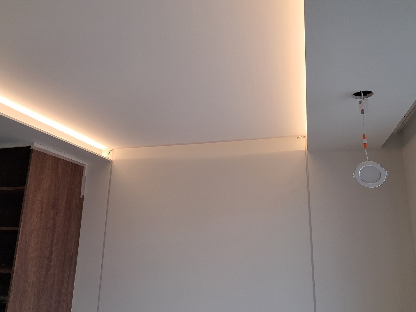 Wnętrze z zamontowanym oświetleniem LED w suficie podwieszanym i oczkiem halogenowym w trakcie instalacji, widoczne przewody i otwór w suficie.