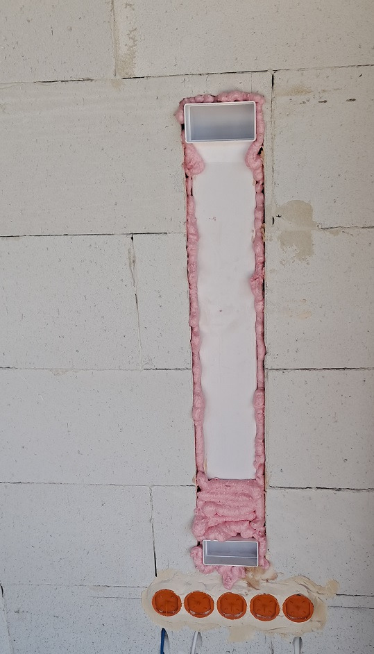 Wnęka w ścianie z betonu komórkowego przygotowana pod instalację elektryczną, zabezpieczona pianką montażową i puszkami instalacyjnymi.