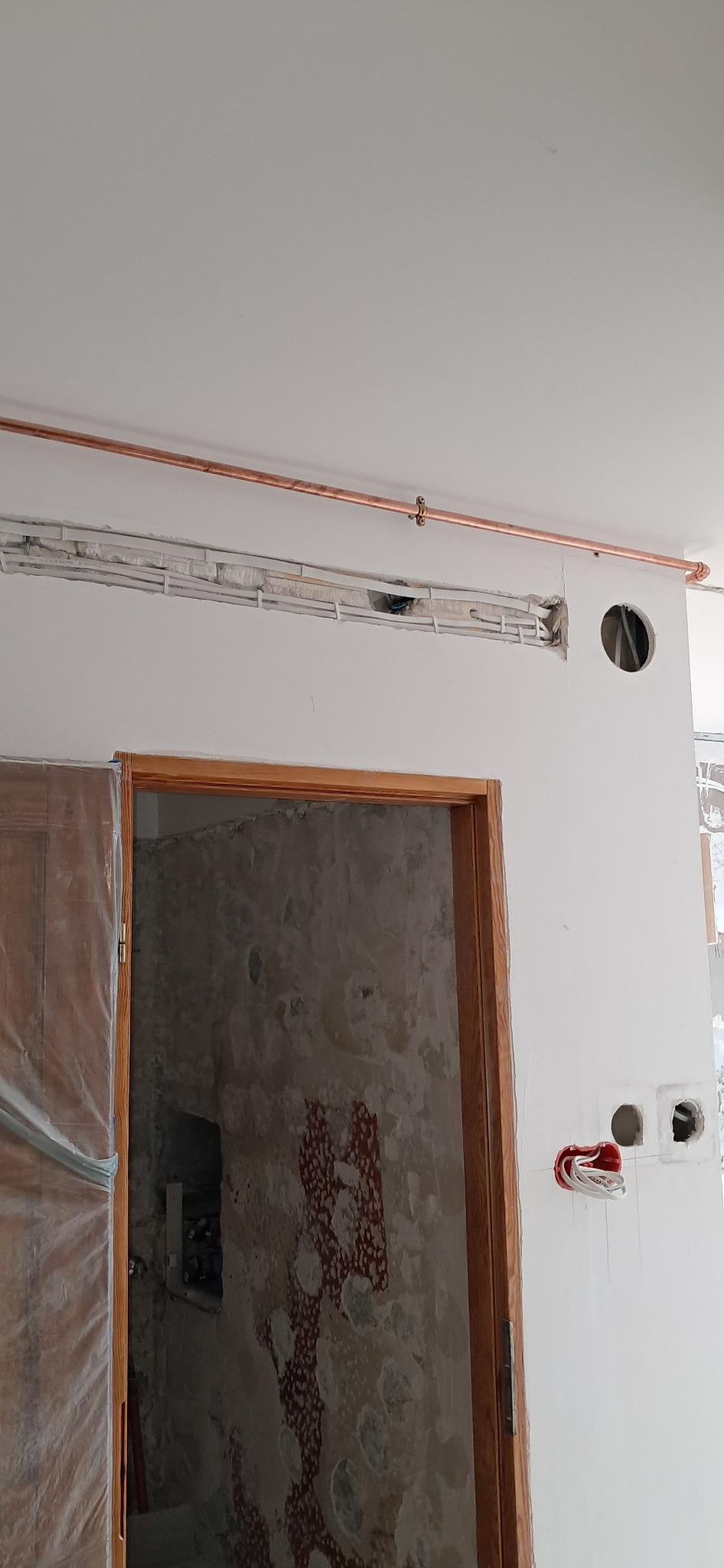 Miedziana rurka i kable w ścianie podczas remontu w Poznaniu. Widoczne otwory na gniazdka i przewody. Ściana w trakcie prac wykończeniowych, widoczny surowy tynk.