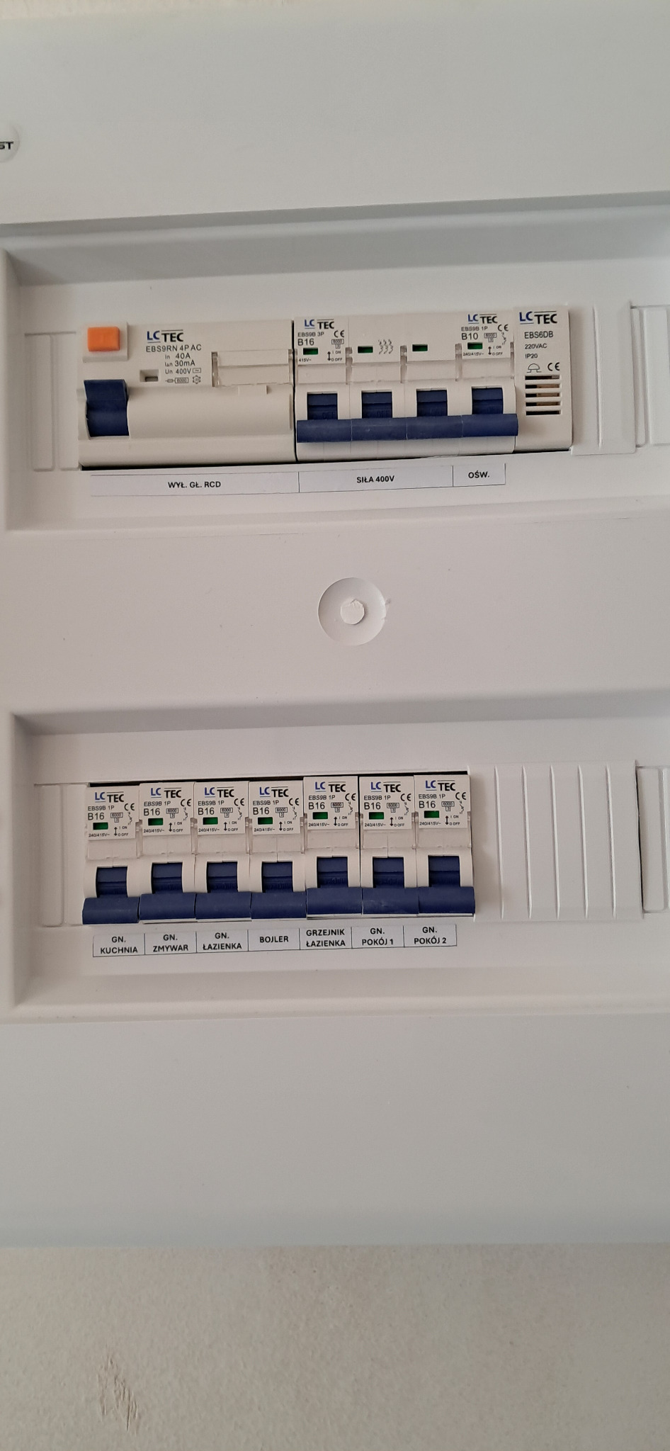 Rozdzielnia elektryczna z bezpiecznikami LC TEC, opisana dla różnych obwodów: kuchnia, zmywarka, łazienka, bojler, grzejnik łazienkowy, pokój 1 i pokój 2.