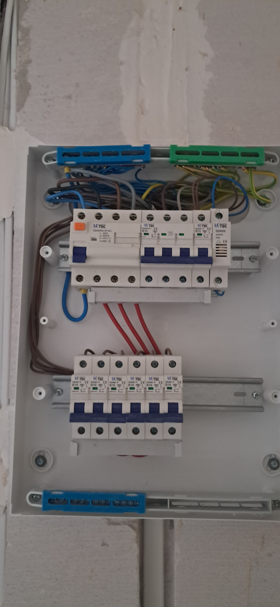 Rozdzielnica elektryczna z zainstalowanymi bezpiecznikami LCTEC, widoczne przewody w różnych kolorach. Biała obudowa na tle surowej ściany.