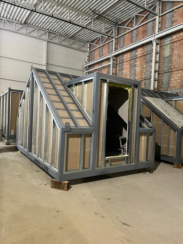 Szkielet modułowej konstrukcji stalowej z wypełnieniem z płyt, częściowo zmontowany, w hali produkcyjnej z widocznym numerem seryjnym na ramie.